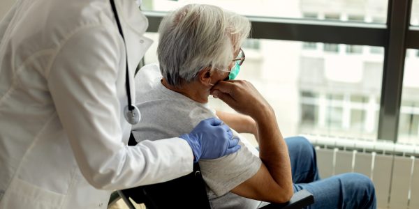 Female doctor consoling senior man in wheelchair during coronavirus lockdown.